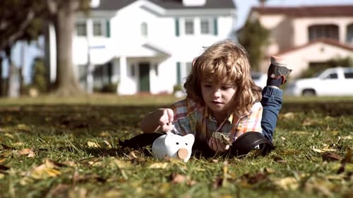 Young Child Saving Money in Piggy Bank on Lawn