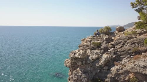 Luftaufnahme eines jungen Mannreisenden auf einer Felsklippe gegen das Meer.