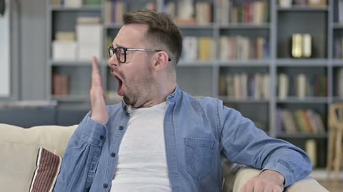 Portrait of Sleepy Young Man Sitting on Sofa and Yawning