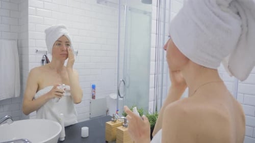 Woman Applies Moisturizer to Face in Bathroom