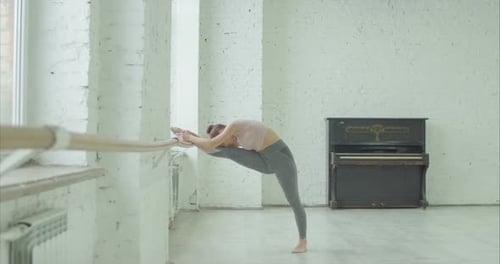 Woman Stretching Legs at Ballet Barre in Studio