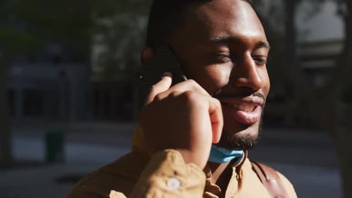 Afroamerikanischer Geschäftsmann mit Gesichtsmaske spricht auf Smartphone