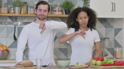 Mixed Race Couple Showing Thumbs Down Sign in Kitchen