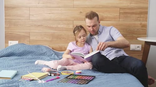 Dad and Daughter Reading Book on Bed at Home