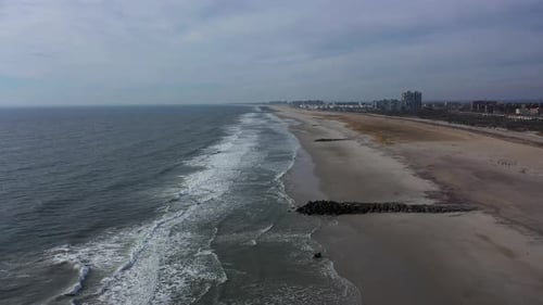 A drone view of an empty beach on a cloudy day. The camera dolly in over the calm waters, as the wav