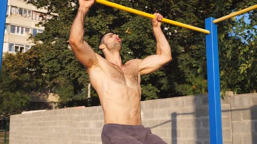 Close Up to Young Muscular Athlete Showing Some Gymnastics Stunts on Horizontal Bar Outdoor