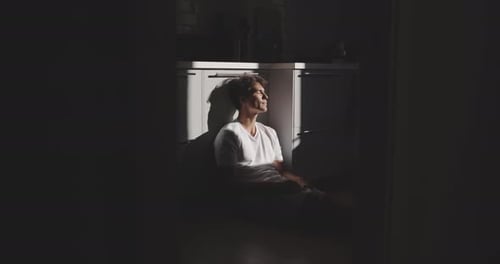 Um menino está sentado no chão pensando e apreciando a luz do sol