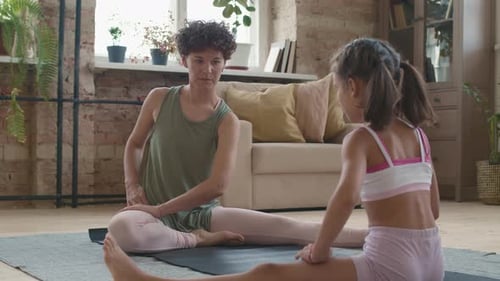 Woman and Girl Stretch Together on Yoga Mat Indoors