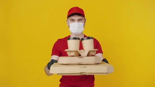 Männlicher Kurier in roter Uniform mit Schutzmaske und Handschuhen, der Mahlzeiten, Bestellung und Kaffee anbietet