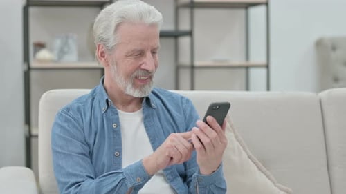 Older Man Smiling Using Phone Indoors
