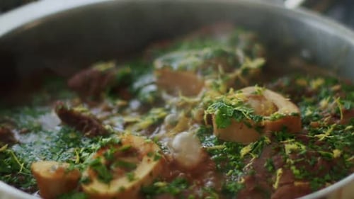 Woman adding lemon zest to stewing ossobuco