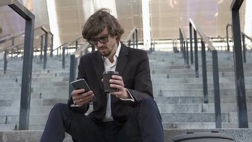 The businessman went out for a coffee break and works on a smartphone.