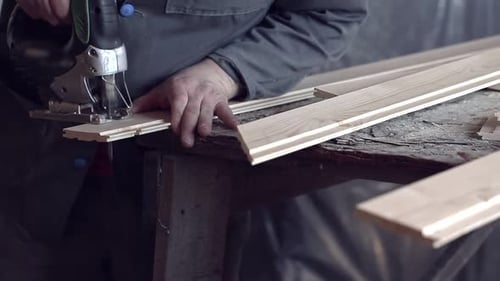 Man Sawing Wooden Plank with Jigsaw at Construction Site