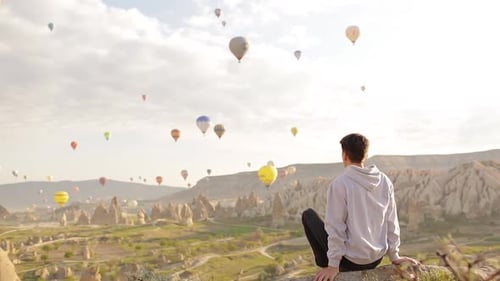 Young Adult Observes Hot Air Balloons Over Landscape