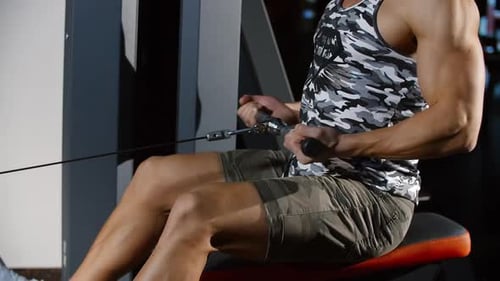 Homme séduisant entraînant des mains et un dos forts faisant de l'exercice sur une machine de sport