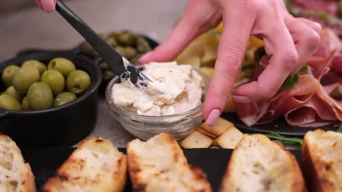 Faire une bruschetta femme étalant du fromage à la crème sur une baguette grillée