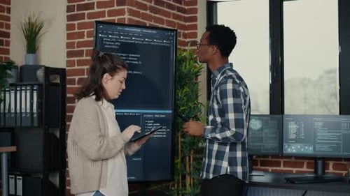 Desenvolvedores de software analisando o código-fonte na TV de tela de parede comparando erros usando tablet digital