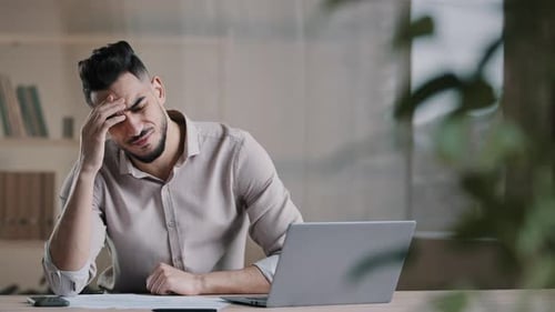 Stressed Young Adult Man At Desk with Laptop
