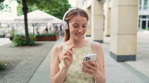 Young Pretty Woman Dancing on Summer Street Wearing Headphones Using Smartphone