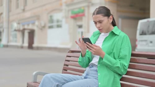 Frustrated Woman Using Smartphone on City Bench