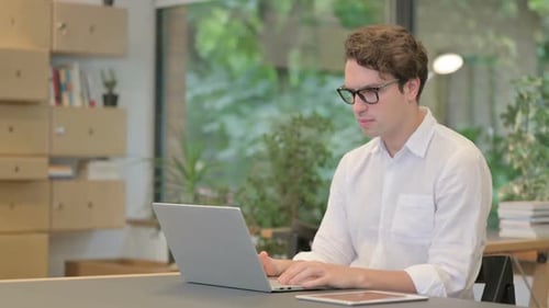 Junger Mann fühlt sich schockiert, als er Laptop im modernen Büro benutzt
