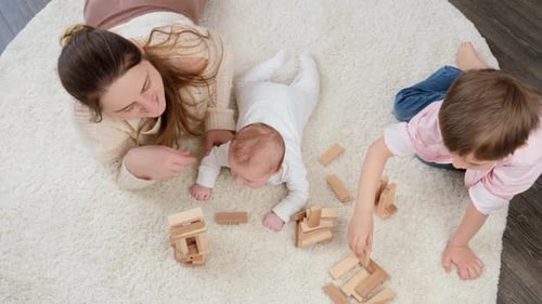 Top View of Mother with Baby and Older Son Playing on Carpet with Toy Wooden Blocks