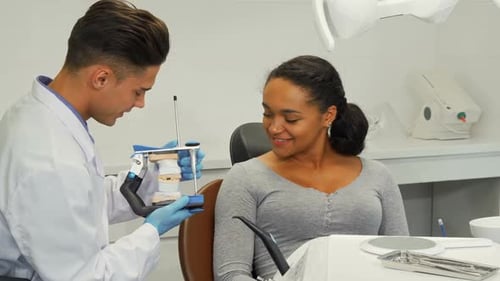Dentist Shows Patient Model of Teeth in Clinic