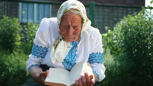 An Old Grandmother is Sitting on the Street and Reading a Book
