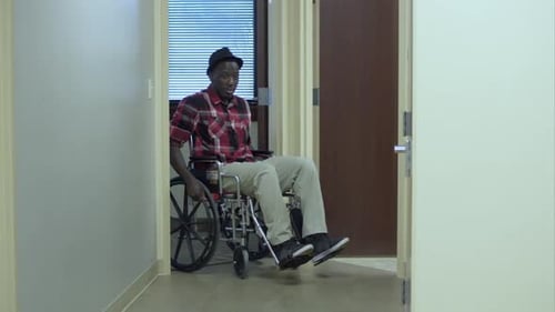 Man Smiles in Wheelchair Rolling Down Hospital Hall