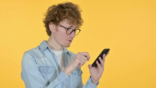 Young Adult Using Smartphone on Yellow Background