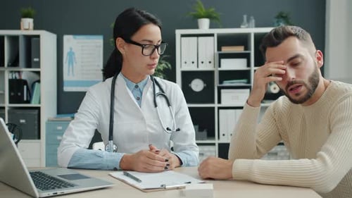 Sick Young Man Getting Bad News in Hospital While Caring Doctor Holding His Hand