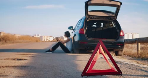 Woman Sitting Aside of Breakdown Vehicle with Warning Triangle Emergency Lights