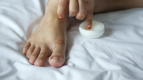 Woman Applying Petroleum Jelly Onto Feet on Bed