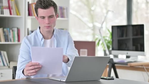 Young Adult Working at Desk with Laptop and Paper