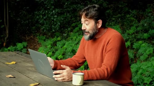 Adult man smile and work with laptop doing online call conference sitting in the nature park