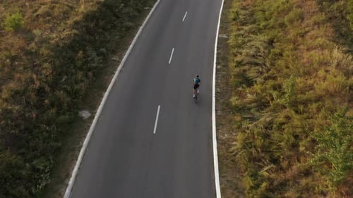 Aerial drone view of man cycling uphill along country road.