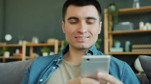 Man Smiles While Using Smartphone Indoors