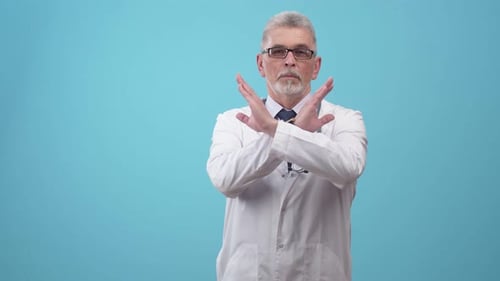 Doctor in a medical uniform with stethoscope shows a sign of the cross with hands in studio