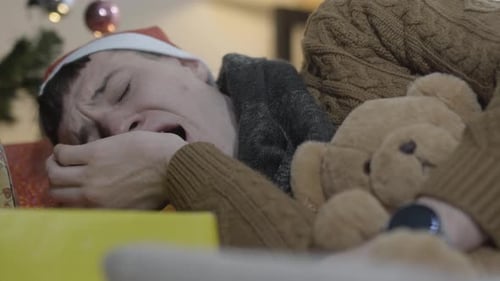 Closeup of Young Man Yawning and Sleeping with Teddy Bear with Decorated Christmas Tree at