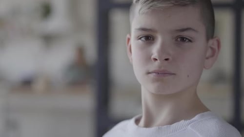 Close Up Portrait of a Young Boy Looking in Camera. The Emotionless Boy in a White T-shirt. Real