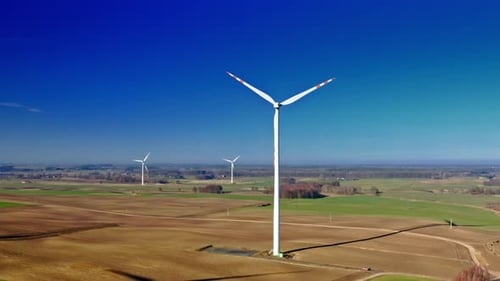Aerial view of white wind turbine with blue sky on brown field