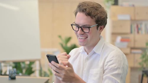 Young Man Celebrates Success While Using Smartphone