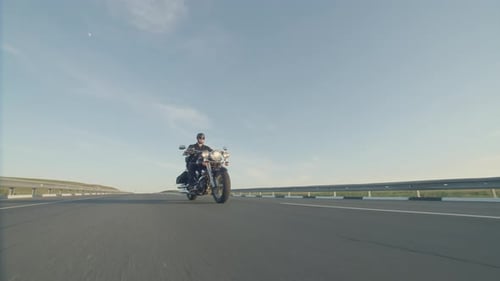 Biker Rushes Along the Highway on Motorbike in Black Helmet and Sunglasses Against Sky and Drives