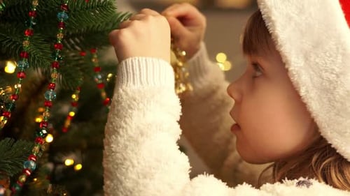 Girl Decorates Christmas Tree with Gold Bell Ornament