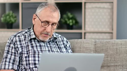 Senior Man Uses Laptop on Couch Indoors