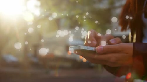 Une femme caucasienne tenant un smartphone sur une rue par une journée ensoleillée avec une animation de bulles lumineuses apparaît lentement