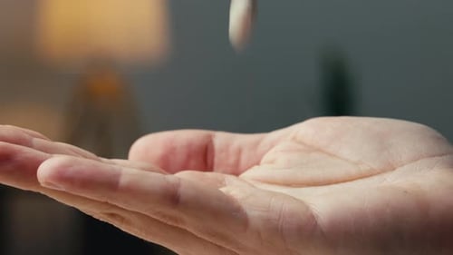 Pill Falling Into a Man's Hand in a Room at Home