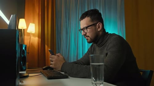 Man Using Mobile Phone at Computer Late at Night