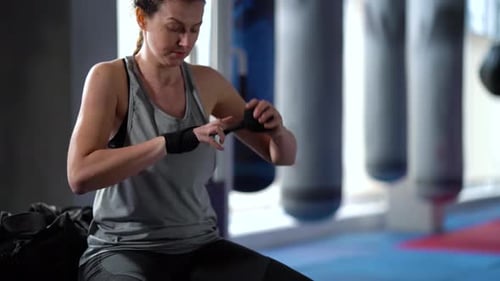 Female Boxer Wrapping Wrists with Bandages Before Training in Gym