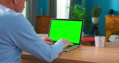 Closeup of a Man Uses Laptop with Green Mockup Screen While Sitting at the Desk
